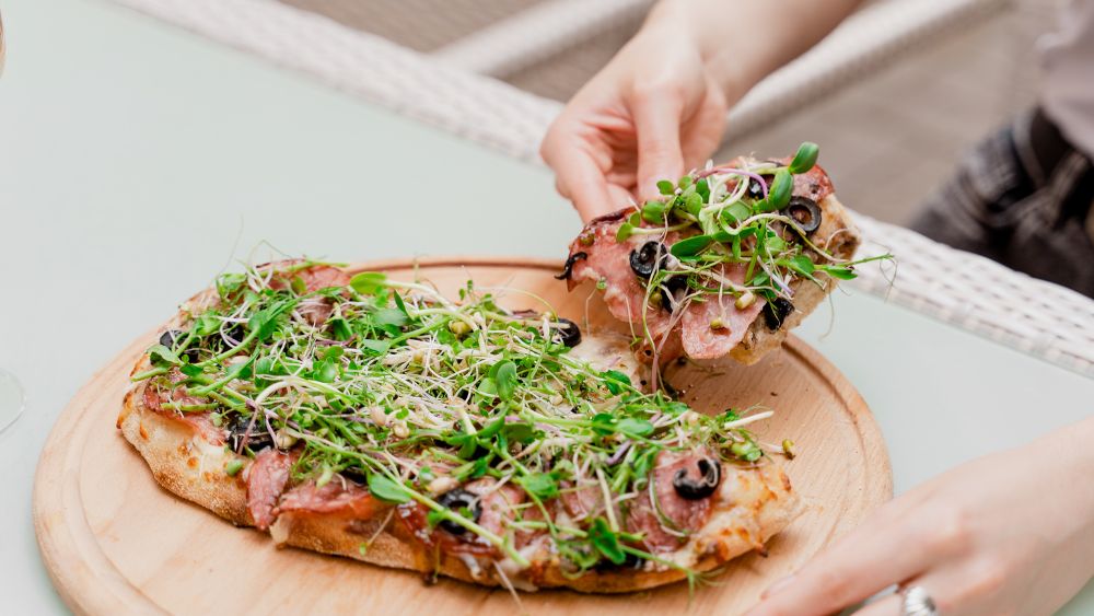 someone holding a slice of pizza topped with microgreens