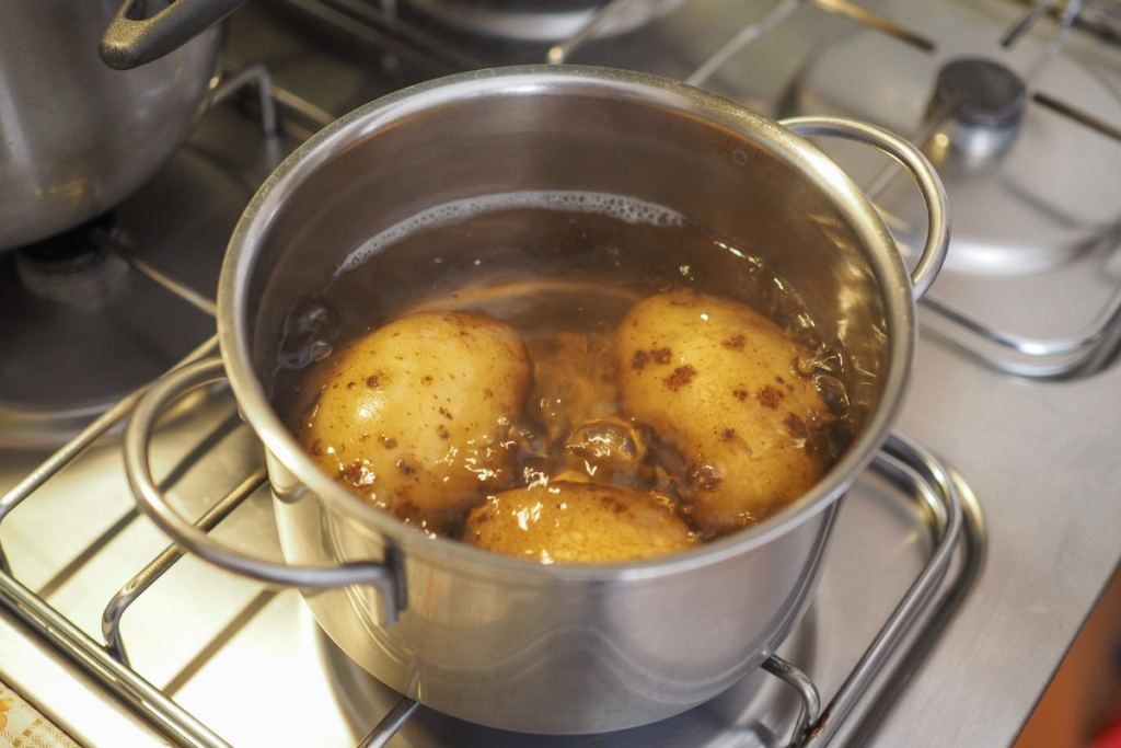 Potatoes boiling in a stainless steel pot on a stovetop, preparing for mashed potato recipe.