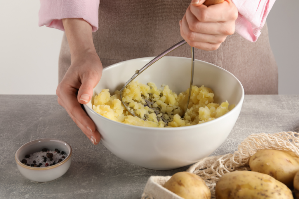 Freshly boiled potatoes being mashed with a hand masher for a creamy holiday mashed potatoes recipe.